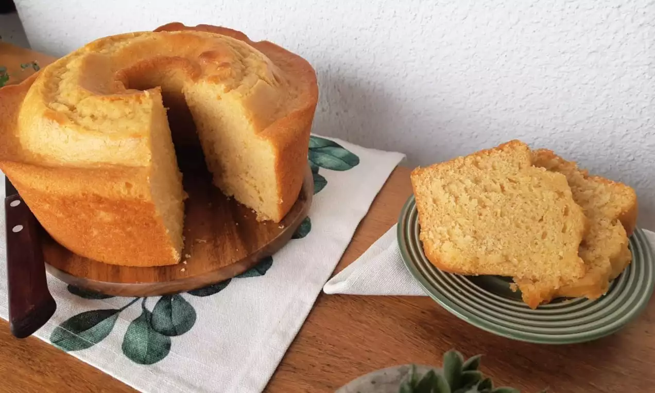 Bolo de milho dourado e macio em forma de anel com textura fofa ao centro, pedaços servidos em prato verde sobre toalha decorada
