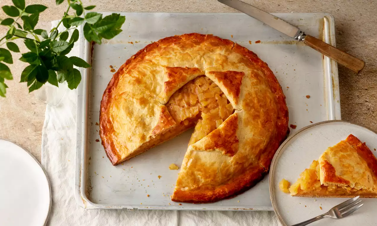 Goldbrauner Apple Pie mit glänzender Kruste, Stück herausgeschnitten, gefüllte Apfelstückchen sichtbar, auf Blech mit Teller und Gabel drapiert