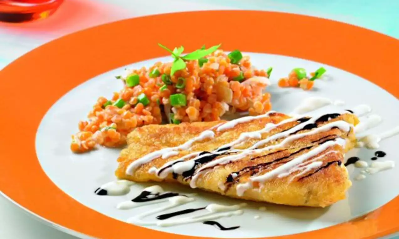 Goldbraunes Pangasiusfilet mit zarten dunklen und weißen Soßenstreifen, daneben orangefarbene Linsen mit grünen Kräutern auf weißem Teller