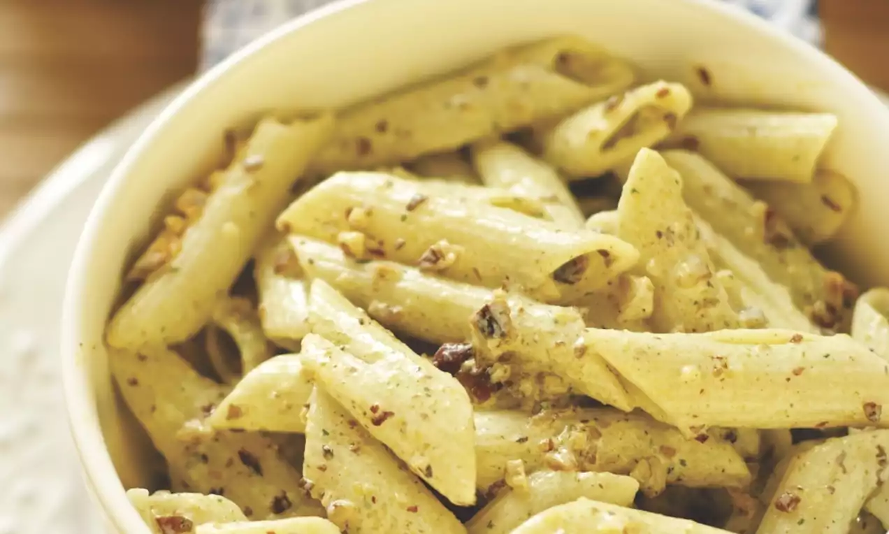 Creamy penne pasta coated in pale golden roasted garlic sauce, speckled with herbs and caramelized garlic pieces in a white bowl