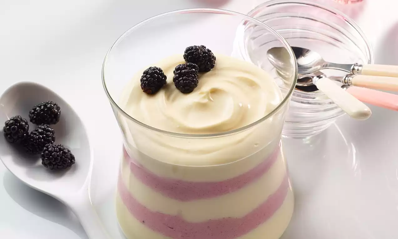 Krema od vanilije u prozirnoj čaši slojevito isprepletena s ružičastim voćnim mousseom, ukrašena crnim kupinama na vrhu