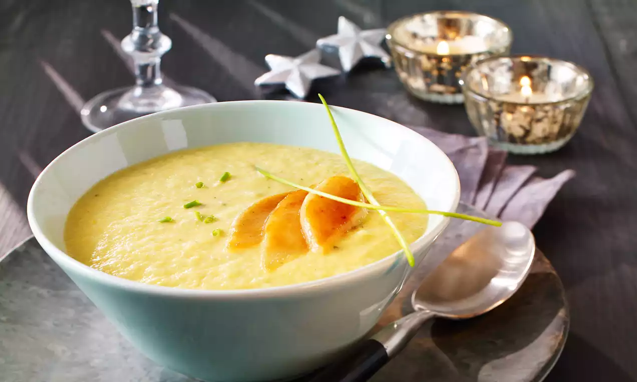 Cremige, gelbliche Pastinakensuppe in einer weißen Schale, garniert mit karamellisierten Birnenscheiben und feinen grünen Schnittlauchstielen