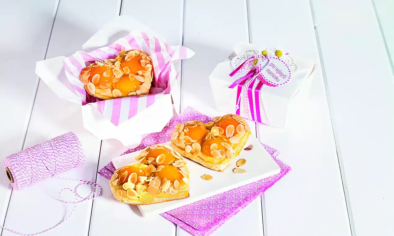 Srdiečka zlatohnedej farby s lesklým povrchom, posypané plátkami mandlí, uložené na bielom tanieri a v pruhovanej papierovej krabičke