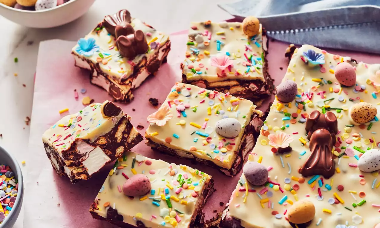 Easter Rocky Road with white chocolate topping, pastel sprinkles, chocolate bunnies, and speckled eggs, cut into squares on pink paper