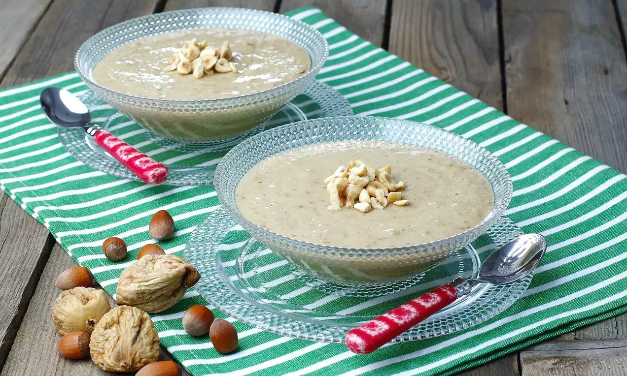 Cam kaselerde sunulan, yüzeyi kıyılmış fındık parçalarıyla süslenmiş, açık bej renkte koyu kıvamlı bir tatlı, yeşil çizgili örtü üzerinde