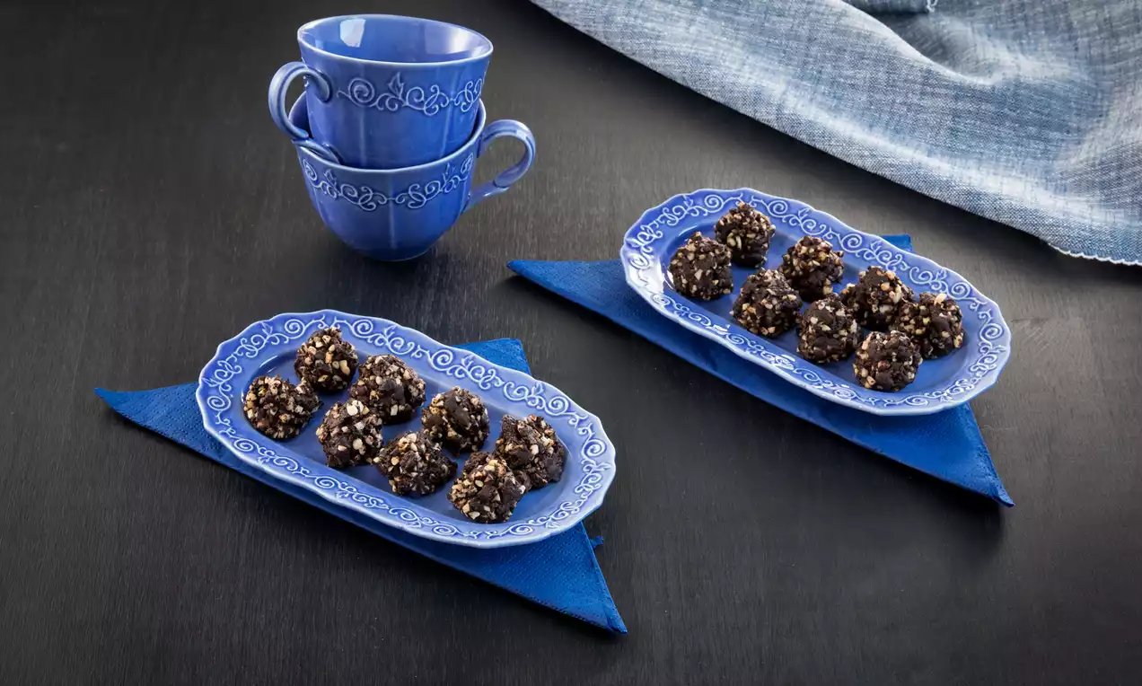 Parlak mavi desenli tabaklarda, koyu çikolata kaplı, kıyılmış fındıklı kayısı topları, koyu fon üzerinde mavi bardaklarla sunulmuş