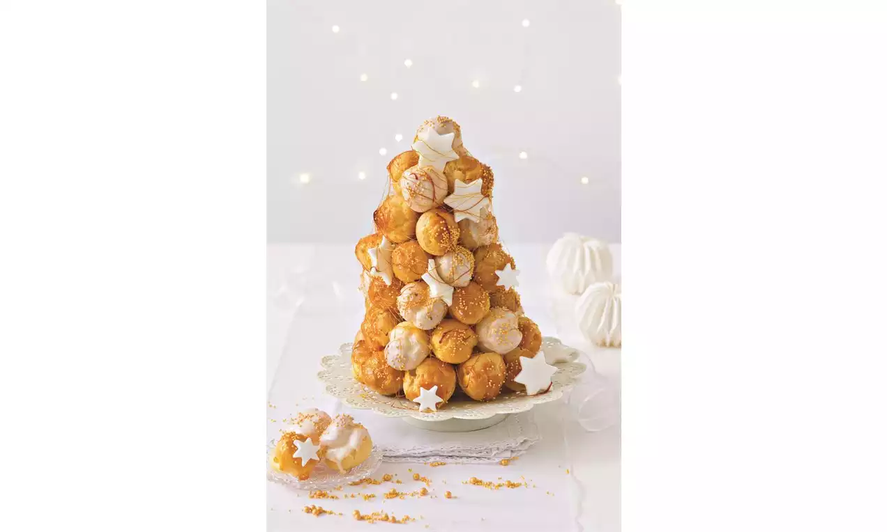 Zlatohnedá croquembouche veža z guľôčok plnených krémom, ozdobená bielymi hviezdami a polevou, na jemne zdobenom porcelánovom tanieri