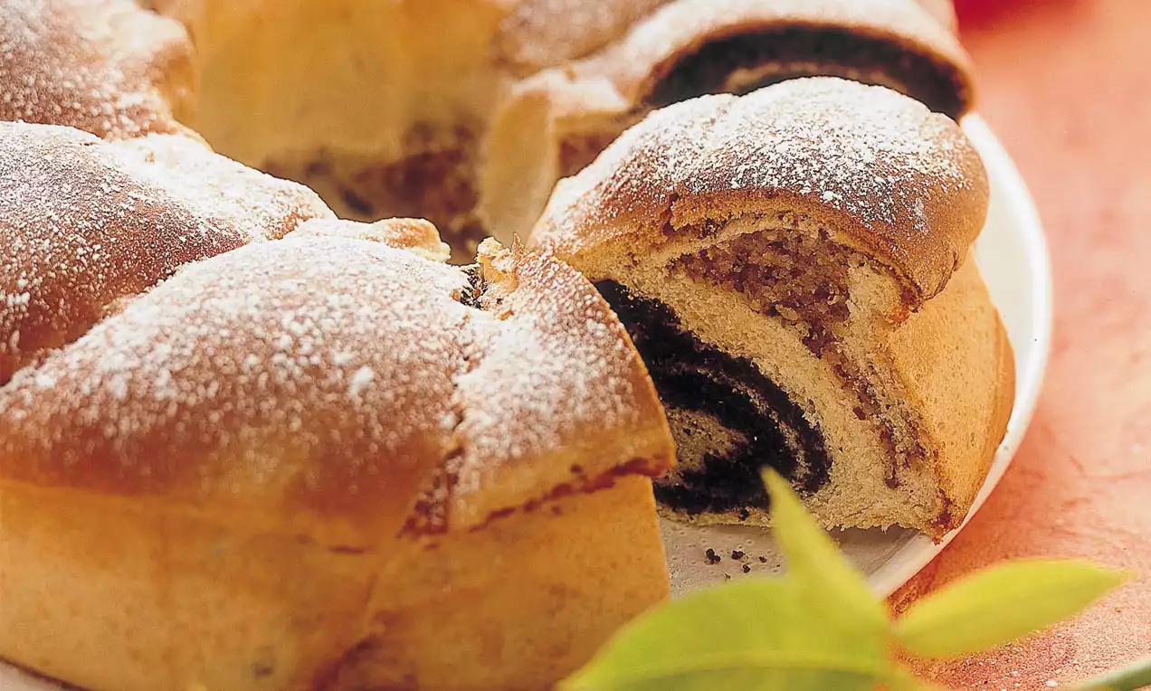 Kranzförmiger Hefekuchen mit goldbrauner Kruste und dunkler Mohnfüllung, leicht mit Puderzucker bestäubt auf einem weißen Teller