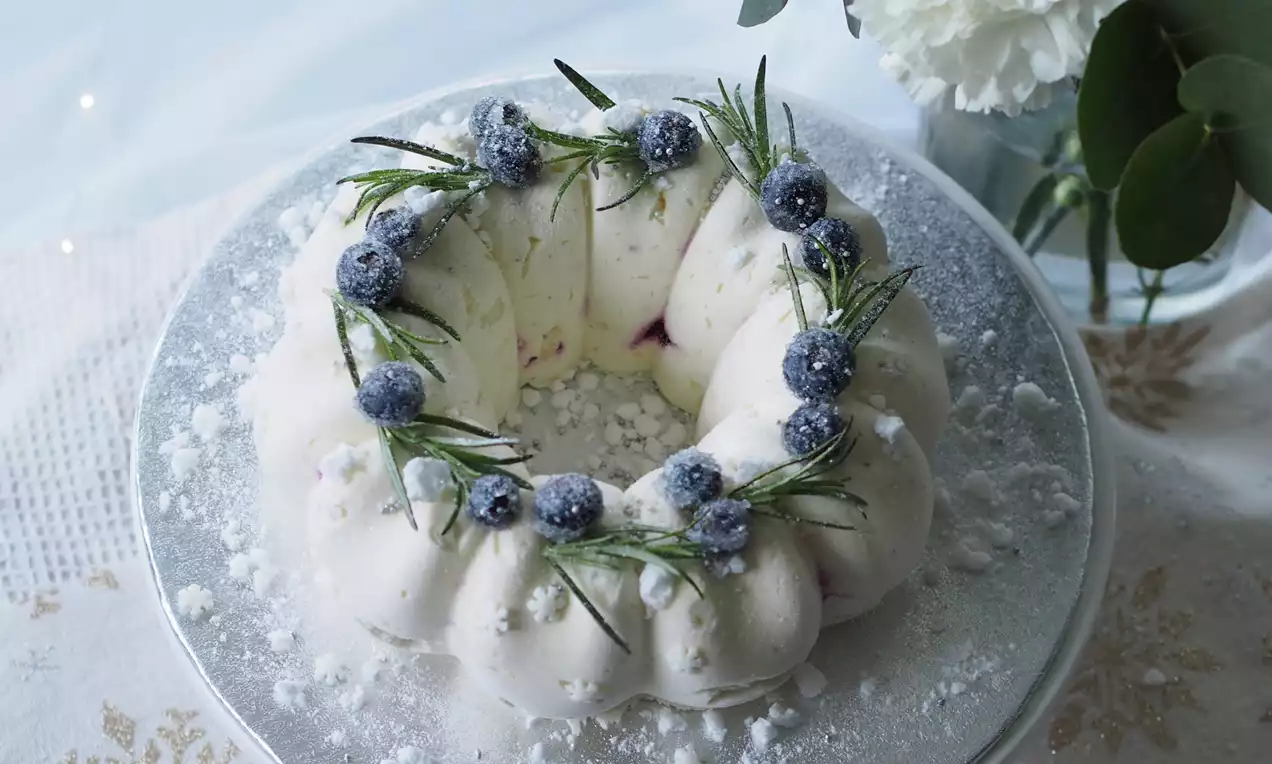 Vaniljanvalkea rengasmaisen jäädykkeen pinta huurteinen, koristeltu sokerilla kuorrutetuilla mustikoilla ja rosmariinin oksilla hopeatarjottimella