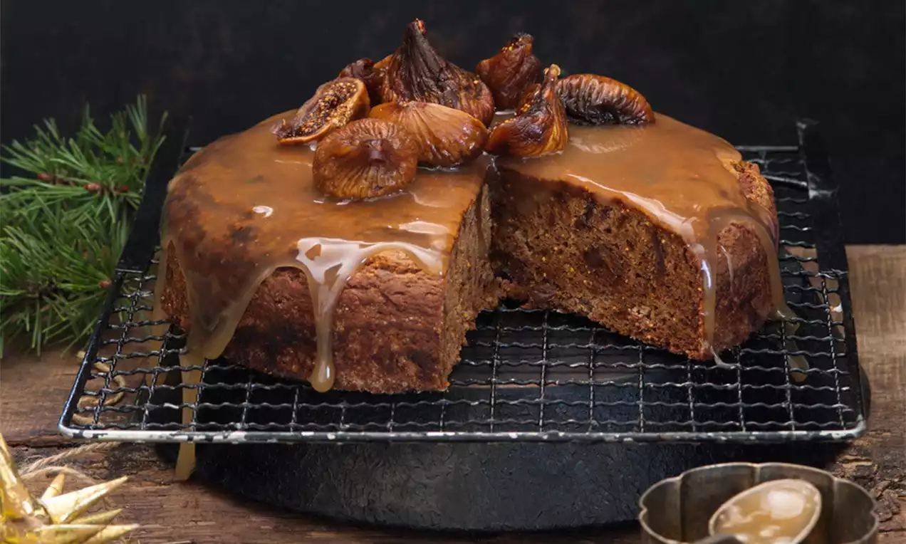 Fíkový dort s karamelovou polevou jemne stekajúci, ozdobený sušenými fígami, položený na kovovej mriežke s vetvičkou jedle na tmavom pozadí