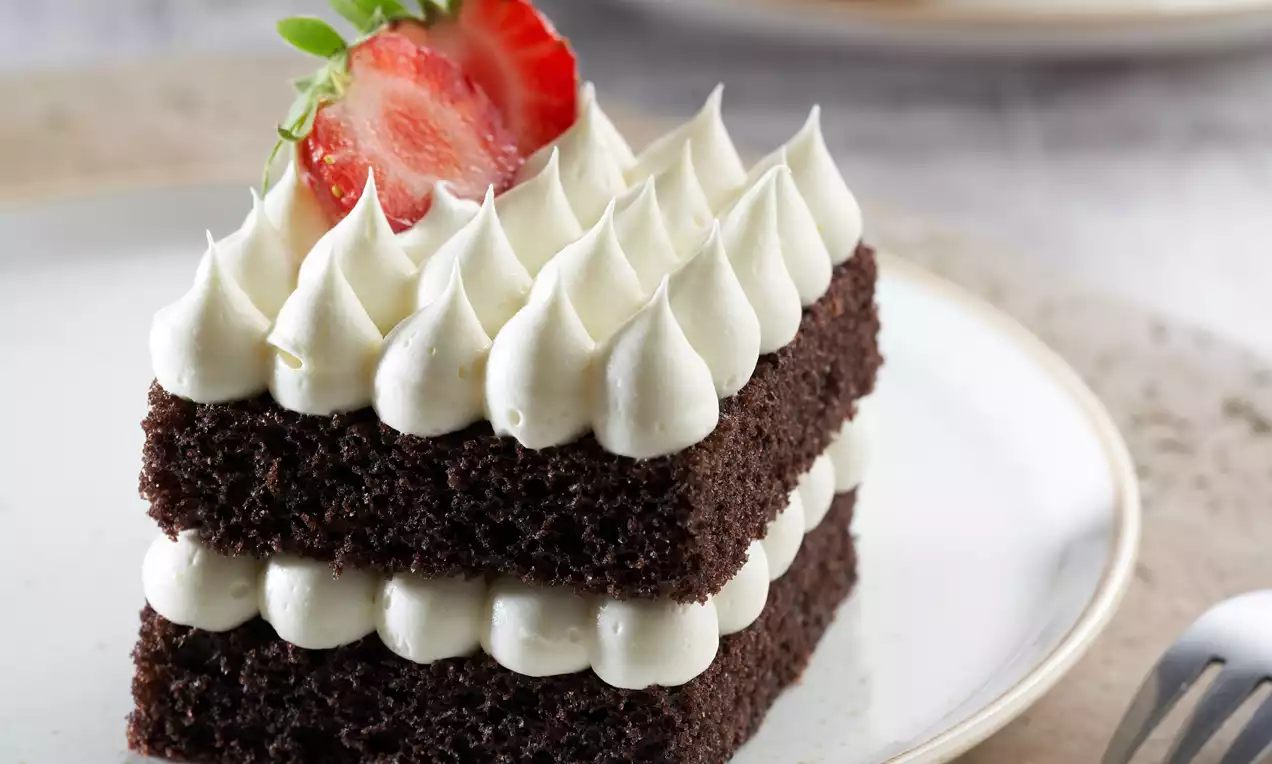 Çikolatalı kek katmanları arasında muzlu puding kreması, üstte krema sıraları ve taze çilekle beyaz tabakta sunulmuş