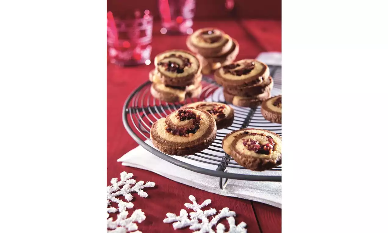 Slimáčiky zlatohnedé s brusnicovou náplňou stočené do špirály, usporiadané na kovovej mriežke na červenom obruse vedľa bielych ozdôb