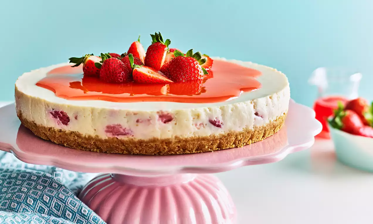 Strawberry cheesecake with a golden biscuit base, creamy filling studded with strawberry pieces, topped with strawberry glaze and fresh berries