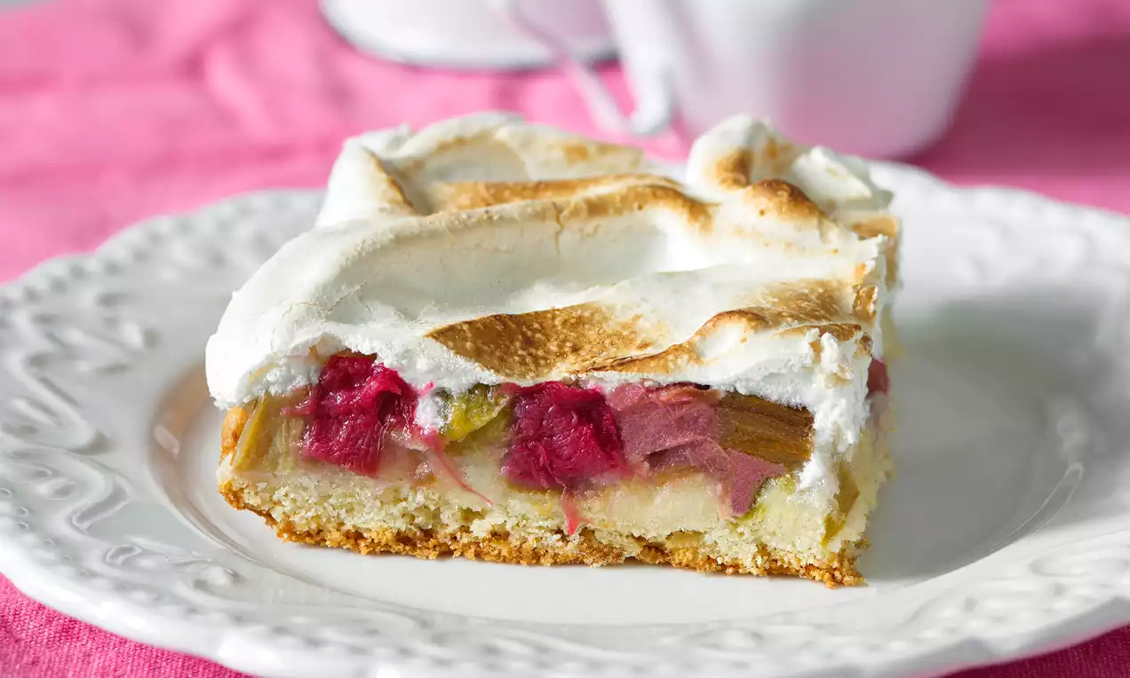 Rebarborový koláč so zlatistou snehovou vrstvou na chrumkavom ceste, s ružovými a zelenkavými kúskami rebarbory, podávaný na bielom tanieri