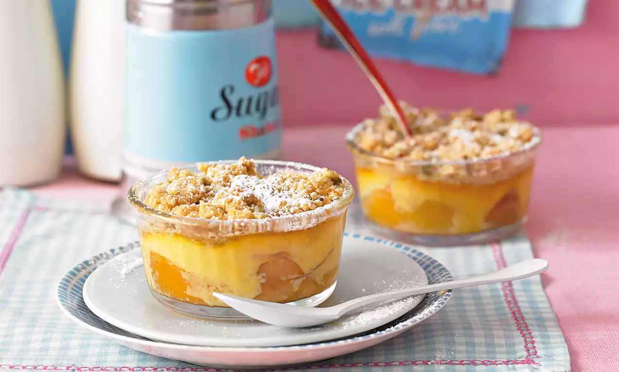 Früchte-Topfen-Crumble mit goldbrauner Streuselkruste, gelber Topfencreme und sichtbaren Fruchtstücken in einem gläsernen Dessertschälchen