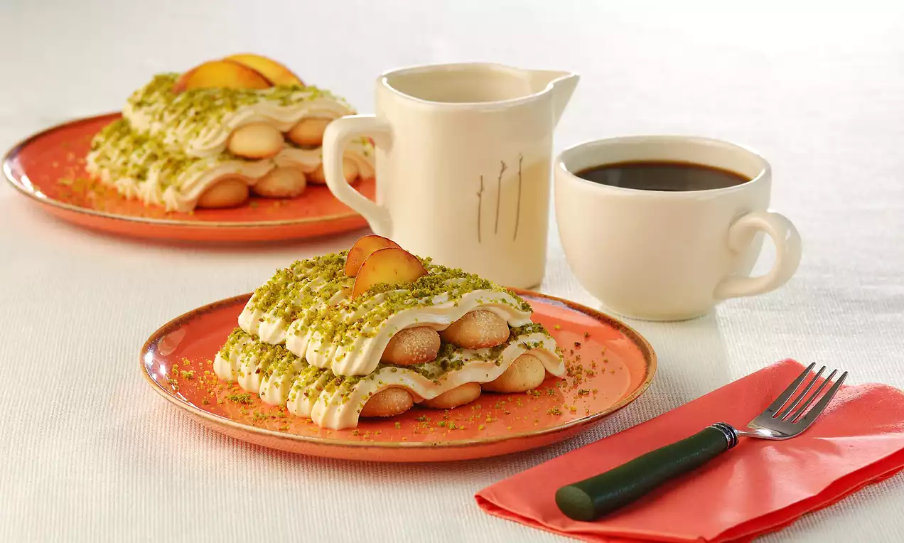 Yeşil çayla ıslatılmış kedi dilleri krema ile kat kat dizilmiş, üzeri Antep fıstığı serpilmiş ve şeftali dilimiyle süslenmiş turuncu tabakta