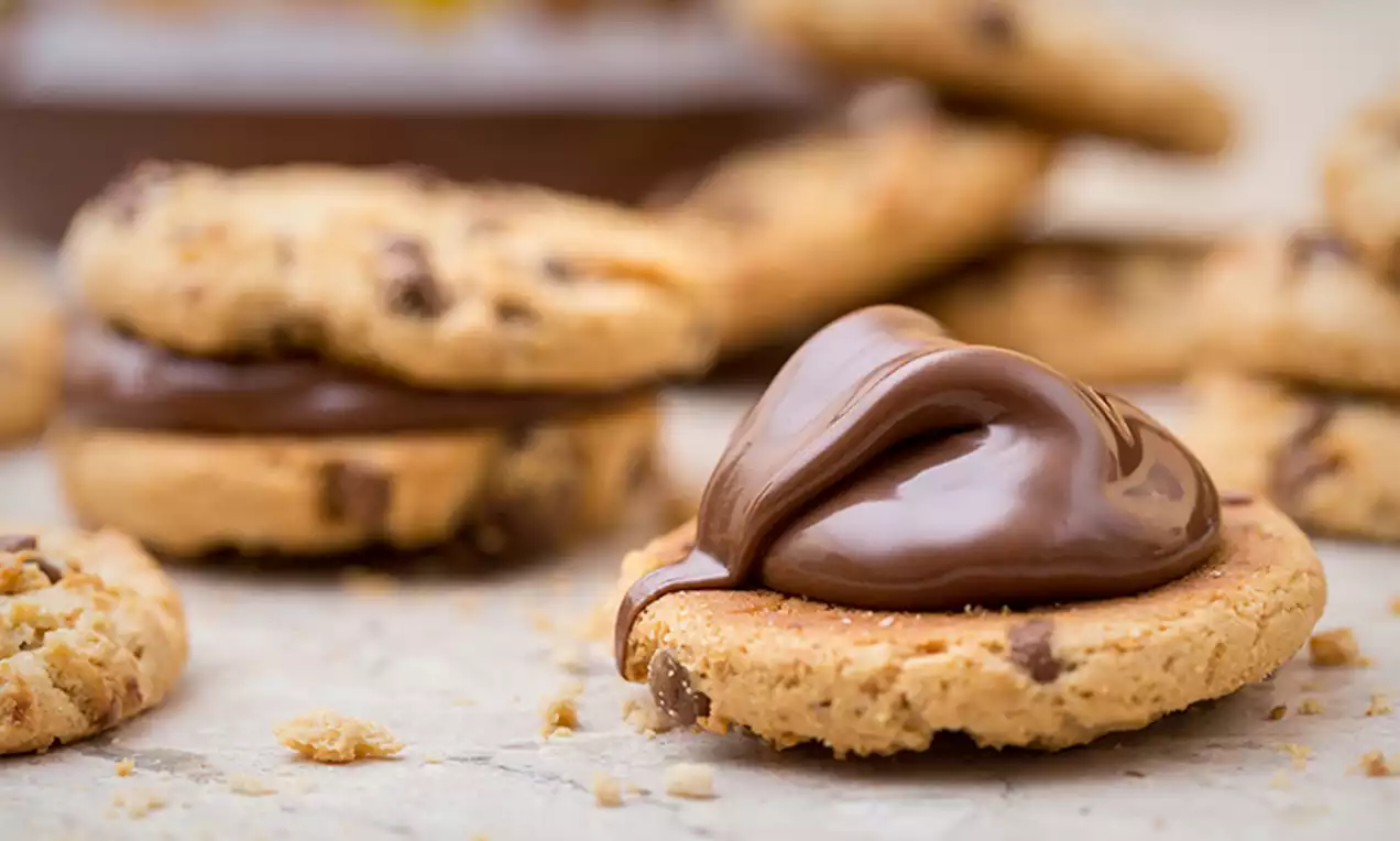 Cookies dorés aux pépites de chocolat garnis de Nutella onctueux formant un tourbillon, disposés sur une surface claire
