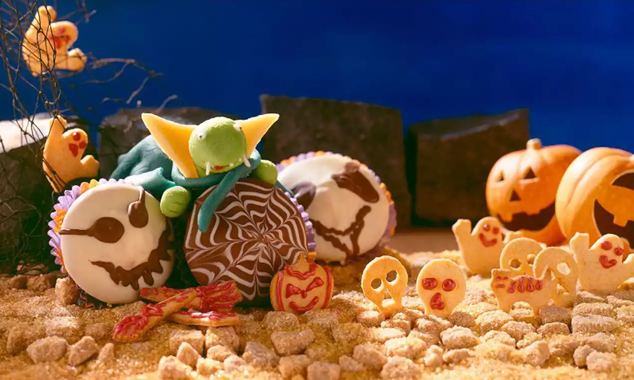 Cupcake au glaçage chocolat marbré entouré de figures fantomatiques, citrouilles sculptées et sable doré sur une table sombre