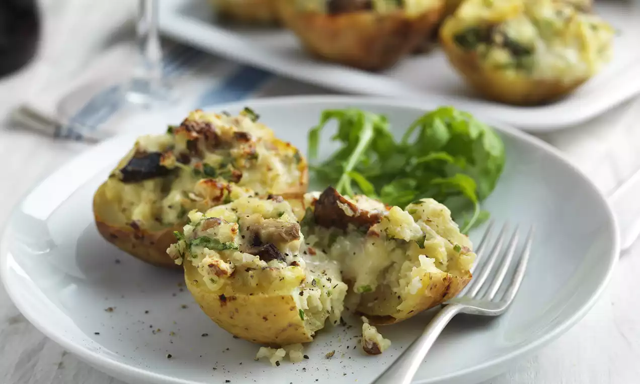 Golden potato skins filled with creamy Gorgonzola, sautéed mushrooms, and chives, served with fresh greens on a white plate