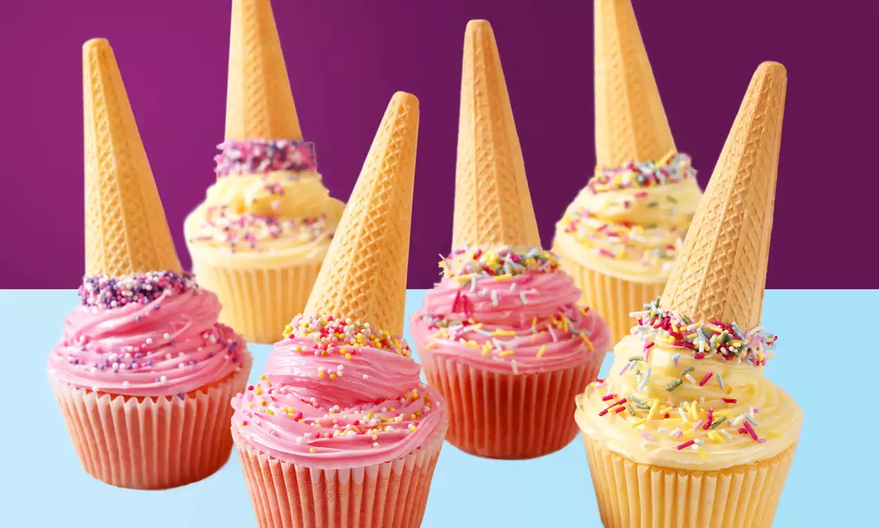 Cupcakes with swirls of pink and yellow frosting, topped with upright wafer cones and colorful sprinkles on a split purple-blue background