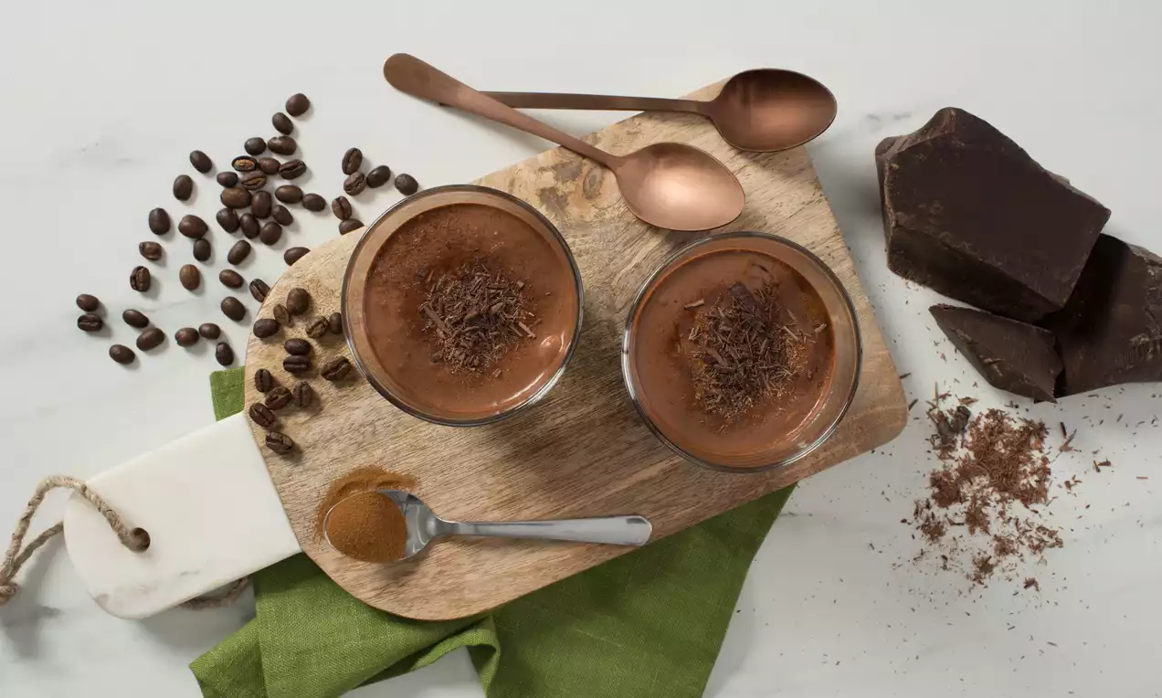 Crèmes chocolat espresso de couleur marron foncé dans des verrines transparentes garnies de copeaux de chocolat sur une planche en bois