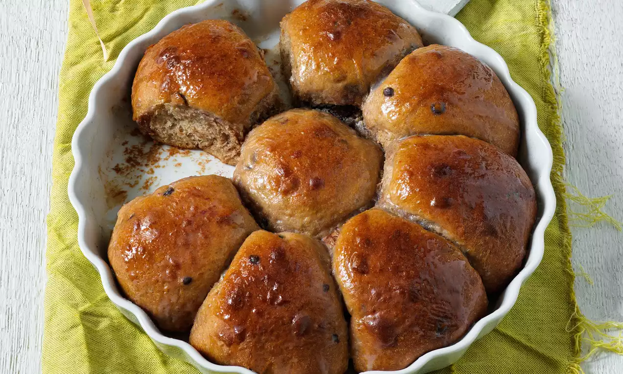 Zlatohnedé trhané buchty s lesklým povrchom, usporiadané do kolieska v bielej zapekacej miske na zelenom látkovom obrúsku