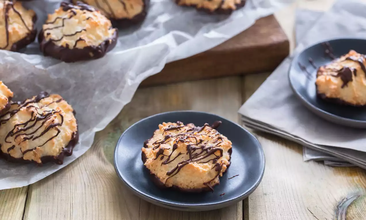 Rochers dorés à la noix de coco aux bords trempés dans du chocolat noir et filetés de chocolat sur des assiettes et du papier cuisson