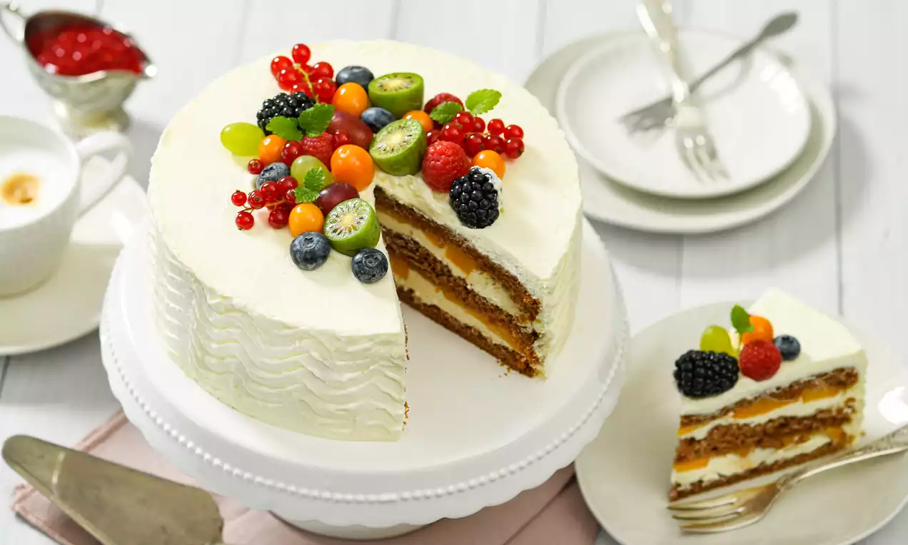 Mascarpone fruit cake with white cream frosting, layers of golden sponge, topped with vibrant berries and fruits, on a white cake stand