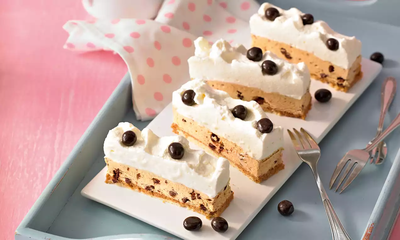 Rechteckige Eiskaffee-Schnitten mit heller Cremeschicht, Schokoladenstückchen und Kaffeebohnen dekoriert auf weißer Platte im rosa Ambiente