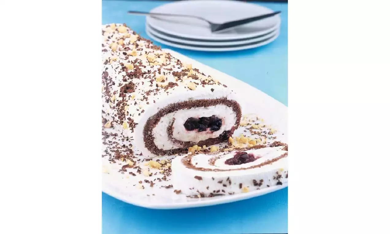 Kakao ve vanilyalı rulo pasta, kremalı dolgu içinde vişne taneleriyle, üstü rende çikolata ve fındık parçalarıyla süslenmiş beyaz tabakta