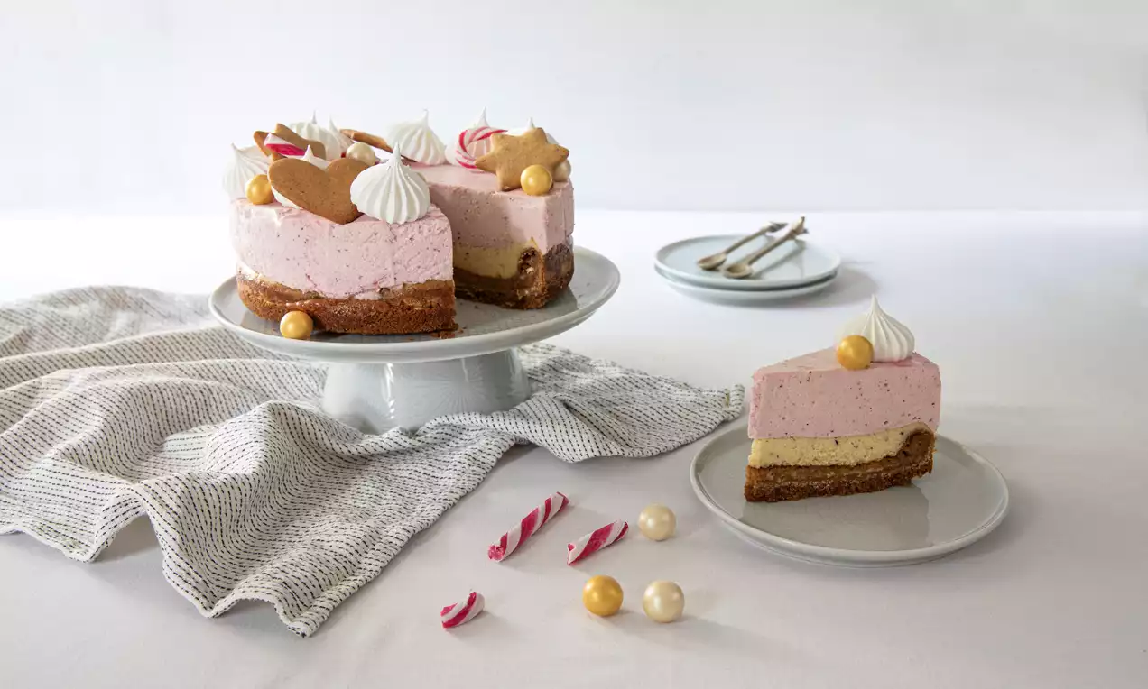 Pinkki kerma täytekakun päällä ruskea pohja, koristeltu piparkakuilla, valkoisilla ja kultaisilla makeilla, asetettu vaalealle jalustalle