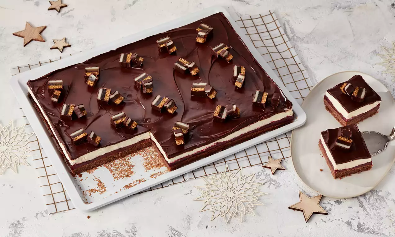 Rechteckiger Dominostein-Kuchen mit dunkler Schokoglasur, weißen Cremeschichten und Dominostein-Stücken auf Blech und Teller angerichtet