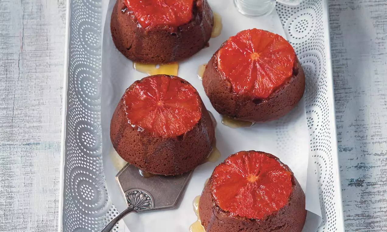 Špaldové tortičky tmavohnedej farby s karamelovou textúrou, dekorované plátkami šťavnatého červeného pomaranča na kovovom podnose