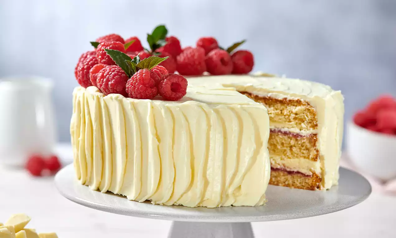 Ganache-Torte mit weißer Creme, schichtweise gefüllt, garniert mit frischen Himbeeren und Minzblättern auf einer weißen Kuchenplatte