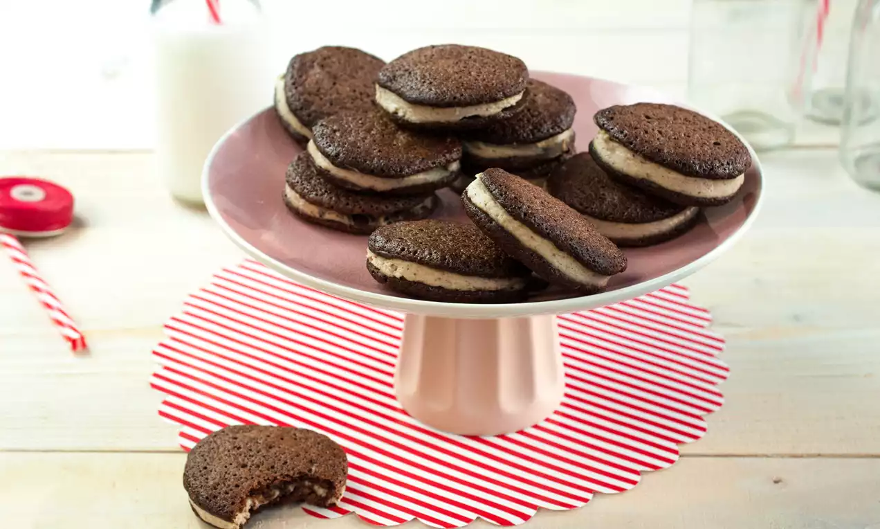 Tmavohnedé okrúhle koláčiky s jemnou krémovou plnkou uložené na ružovom podnose so svetločervenou pruhovanou dekoráciou pod tanierom