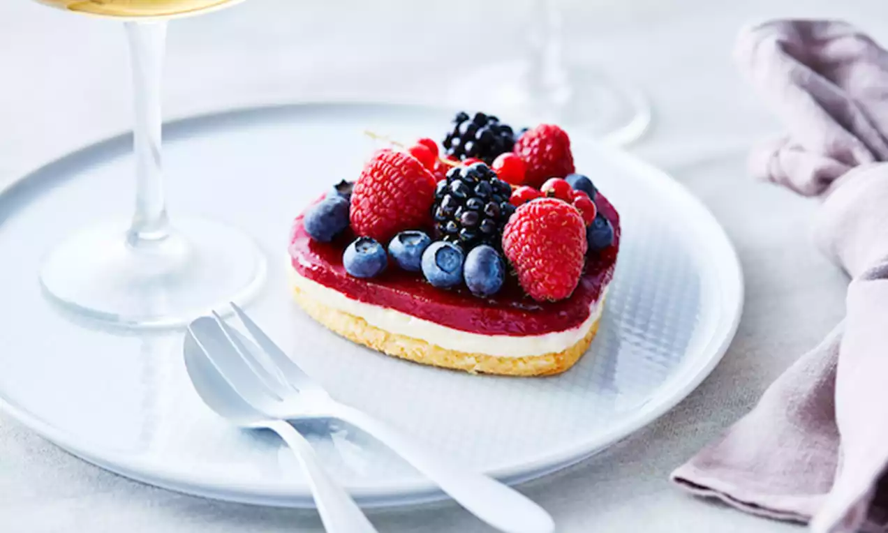 Tartelette aux fruits rouges garnie de framboises, myrtilles et mûres sur un fond sablé doré, présentée sur une assiette blanche