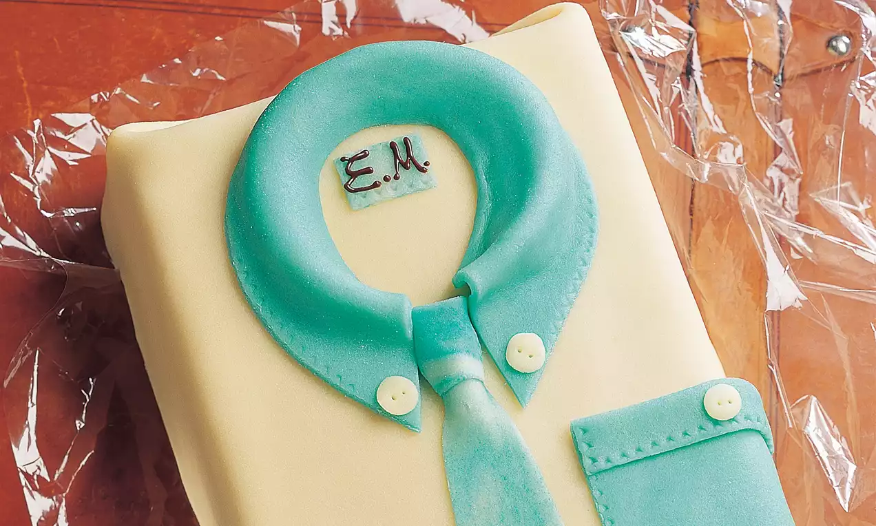Rechteckige Torte eingedeckt mit cremefarbener Fondant-Decke, darüber helltürkises Hemd aus Zucker, verziert mit Kragen und Knöpfen