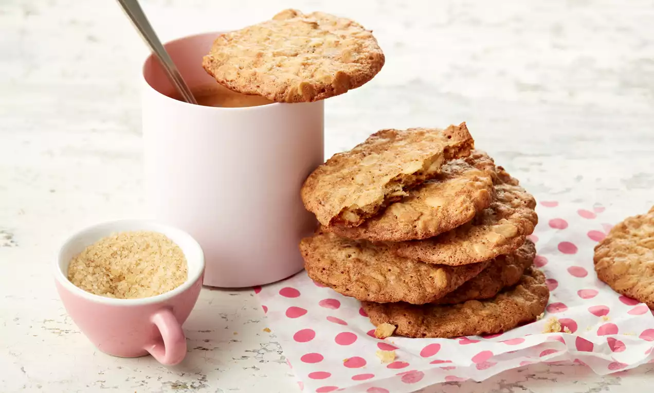 Goldbraune, knusprige Haferflockenplätzchen in unregelmäßiger Form, gestapelt auf einem gepunkteten Serviettenpapier mit rosa Tasse und Schälchen
