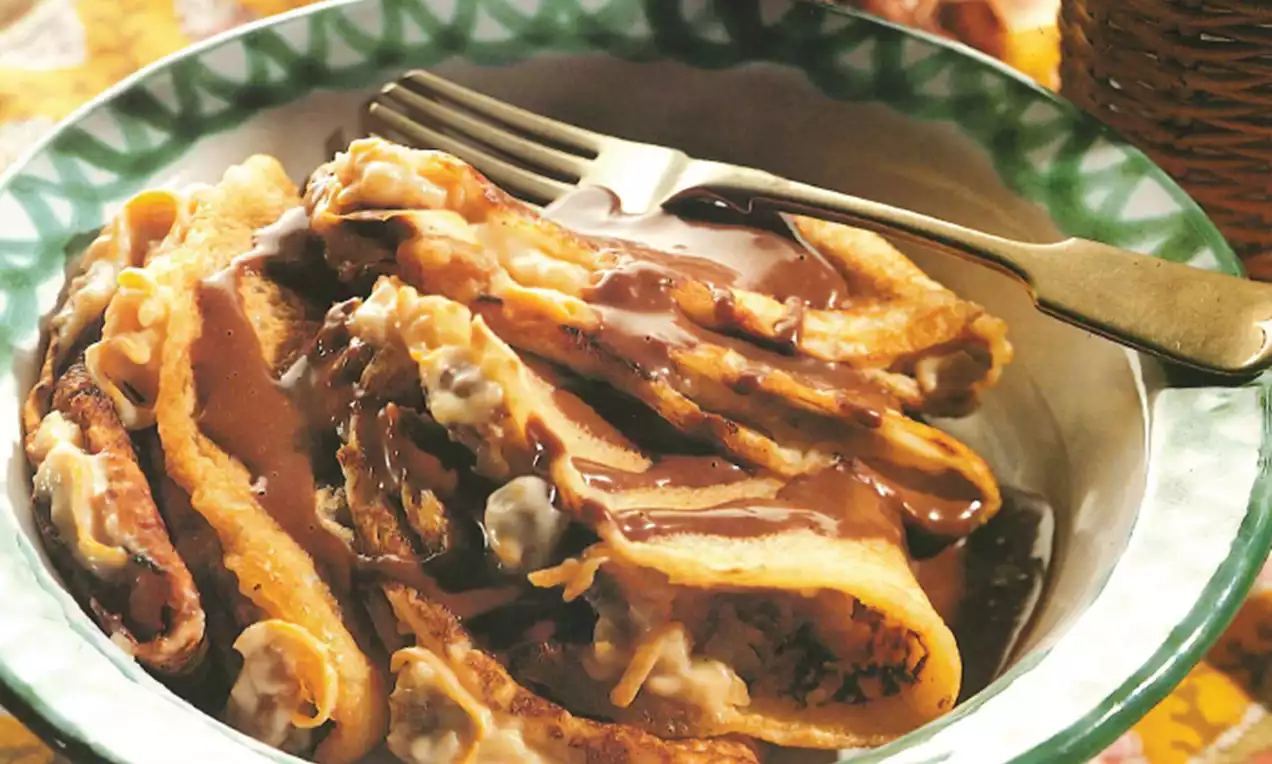 Goudbruine Hongaarse flensjes met vouwen, besprenkeld met glanzende chocoladesaus en geserveerd in een witgroen bord met een vork