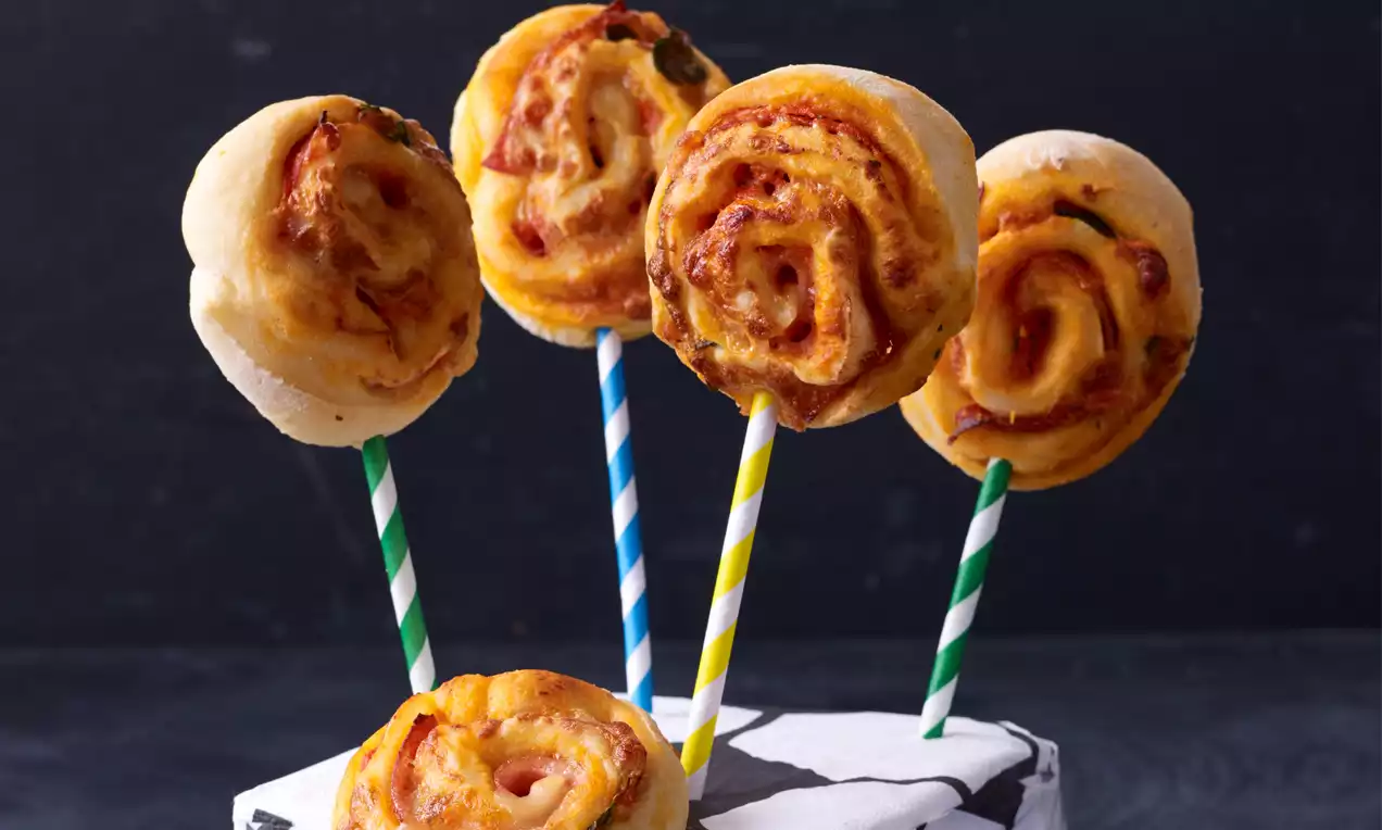 Goldbraune, spiralförmige Pizza-Lollis mit geschmolzenem Käse und Tomatensoße auf bunten Stielen, arrangiert auf weißem Sockel
