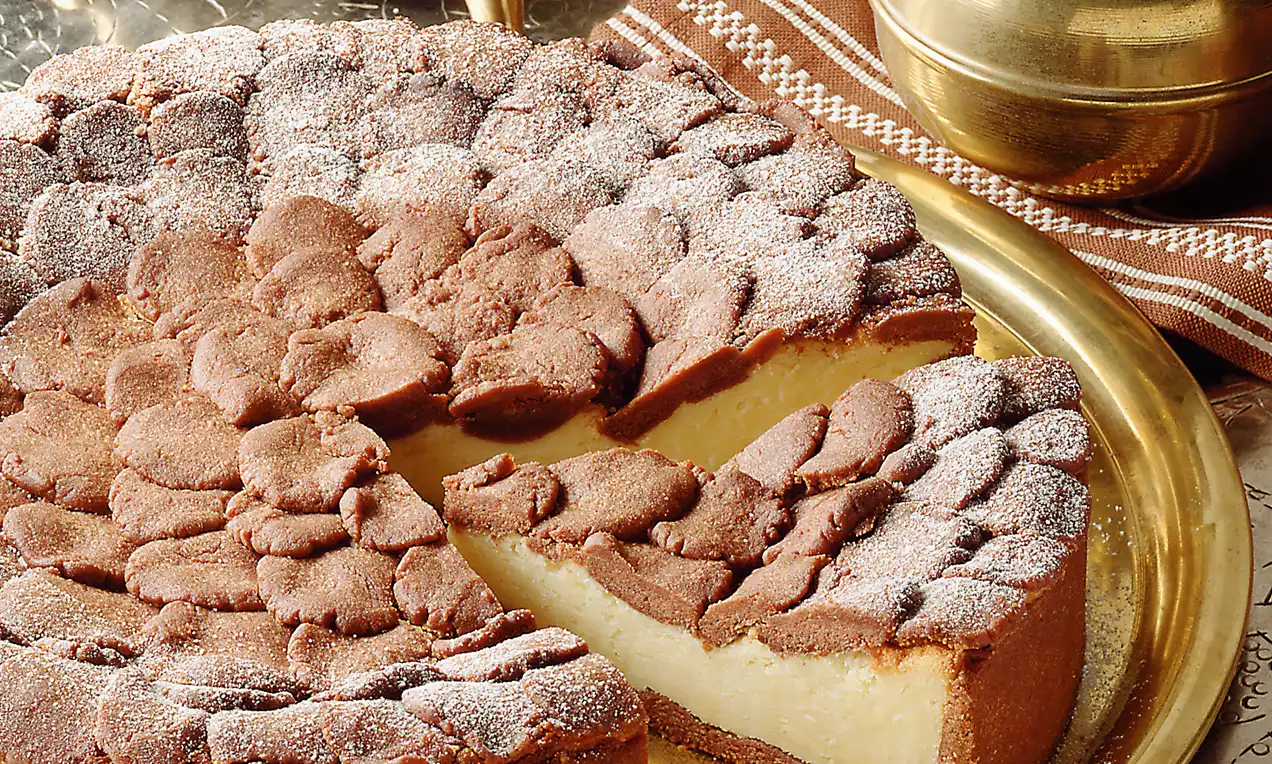 Russische Zupftorte mit dunkelbraunem Kakaoteig und zartgelber Füllung auf einem goldenen Teller, bestäubt mit Puderzucker, neben einem Samowar