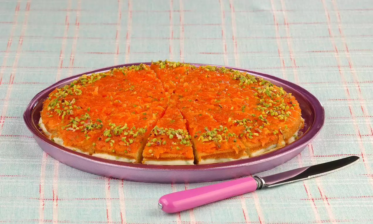 Turuncu havuç dilimleri kat kat dizilmiş, üzeri ince dövülmüş yeşil fıstıklarla süslenmiş, mor tabakta dilimlenmiş şekilde sunulmuş