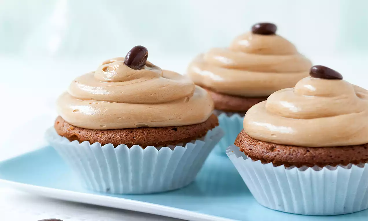 Nougat-Cupcakes mit schokoladigem Teig, zarter Nougatcremehaube und dekorativen Schoko-Kaffeebohnen in pastellblauen Papierförmchen