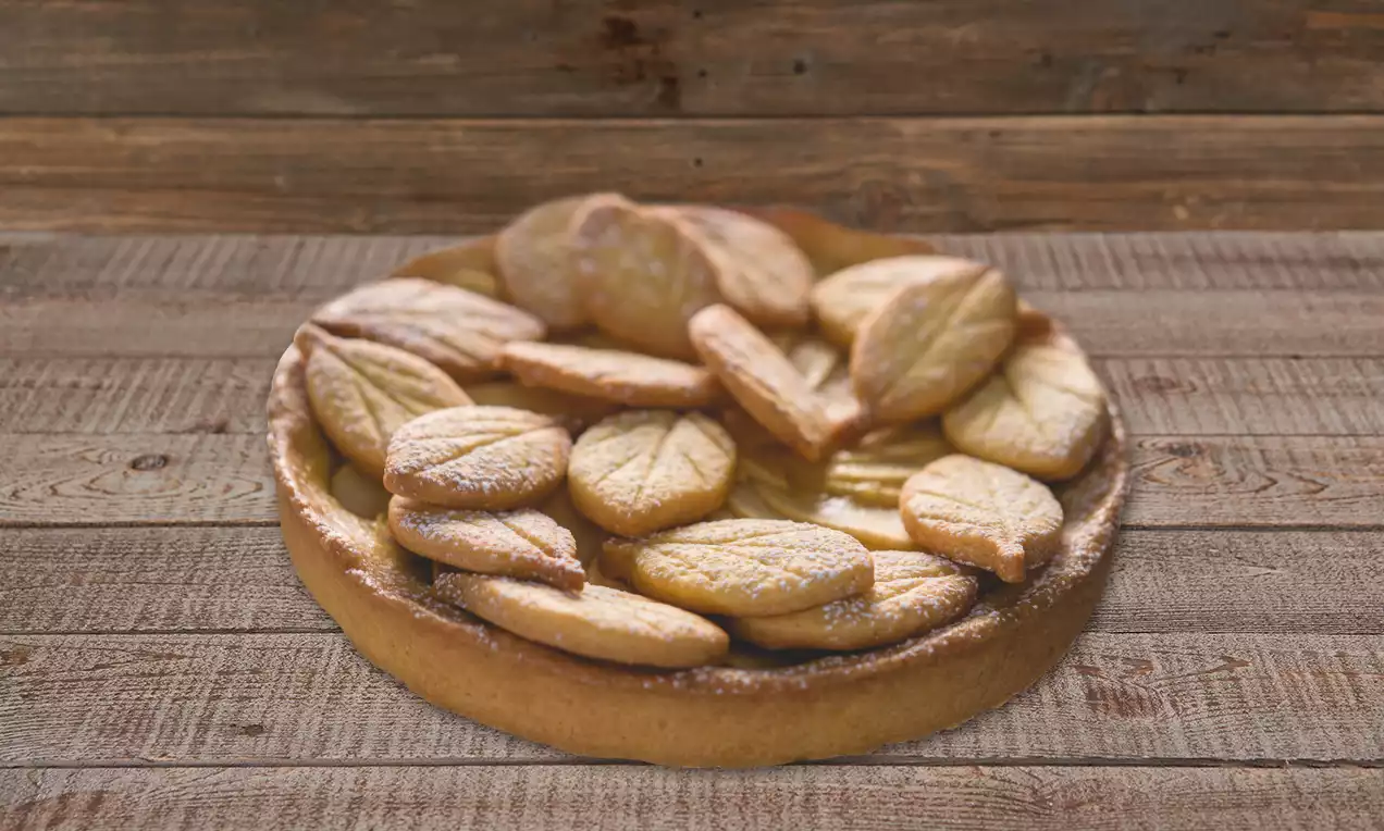 Crostata dai toni dorati con superficie decorata da biscotti a forma di foglia, spolverati di zucchero a velo, su una base di legno