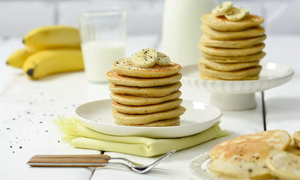 Zlatisté lievance usporiadané do vysokých komínikov, ozdobené plátkami banánu a posypané mletým korením na bielom tanieri s jemným podkladom servítky