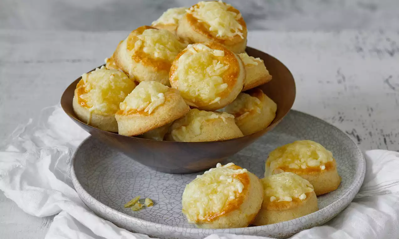 Sýrové pagáče zlatavě hnědé, nadýchané a kulaté, s lesklou sýrovou vrstvou nahoře, vyskládané v tmavé misce na šedém talíři s látkovou dekorací