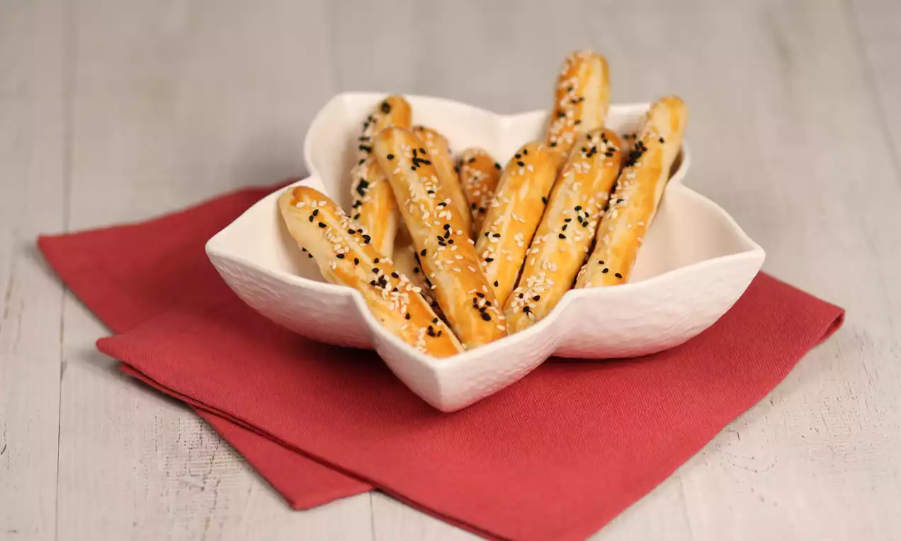 Altın rengi üzeri susam ve çörek otuyla kaplı çıtır tuzlu çubuklar kırmızı bir peçete üzerinde beyaz çiçek formunda bir tabakta