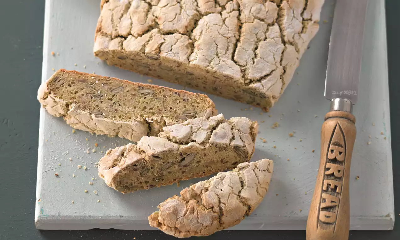 Glutenfreies Brot mit heller, rustikal aufgebrochener Kruste, in dicke Scheiben geschnitten, angerichtet auf einem hellen Holzbrett mit Messer