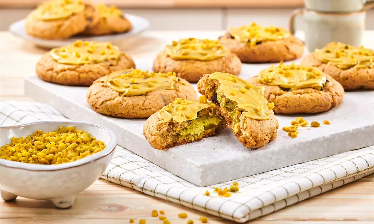 Pistazien-Cookies mit goldbrauner Kruste, weicher grüner Füllung und gelber Creme, auf Steinplatte und kariertem Tuch angerichtet