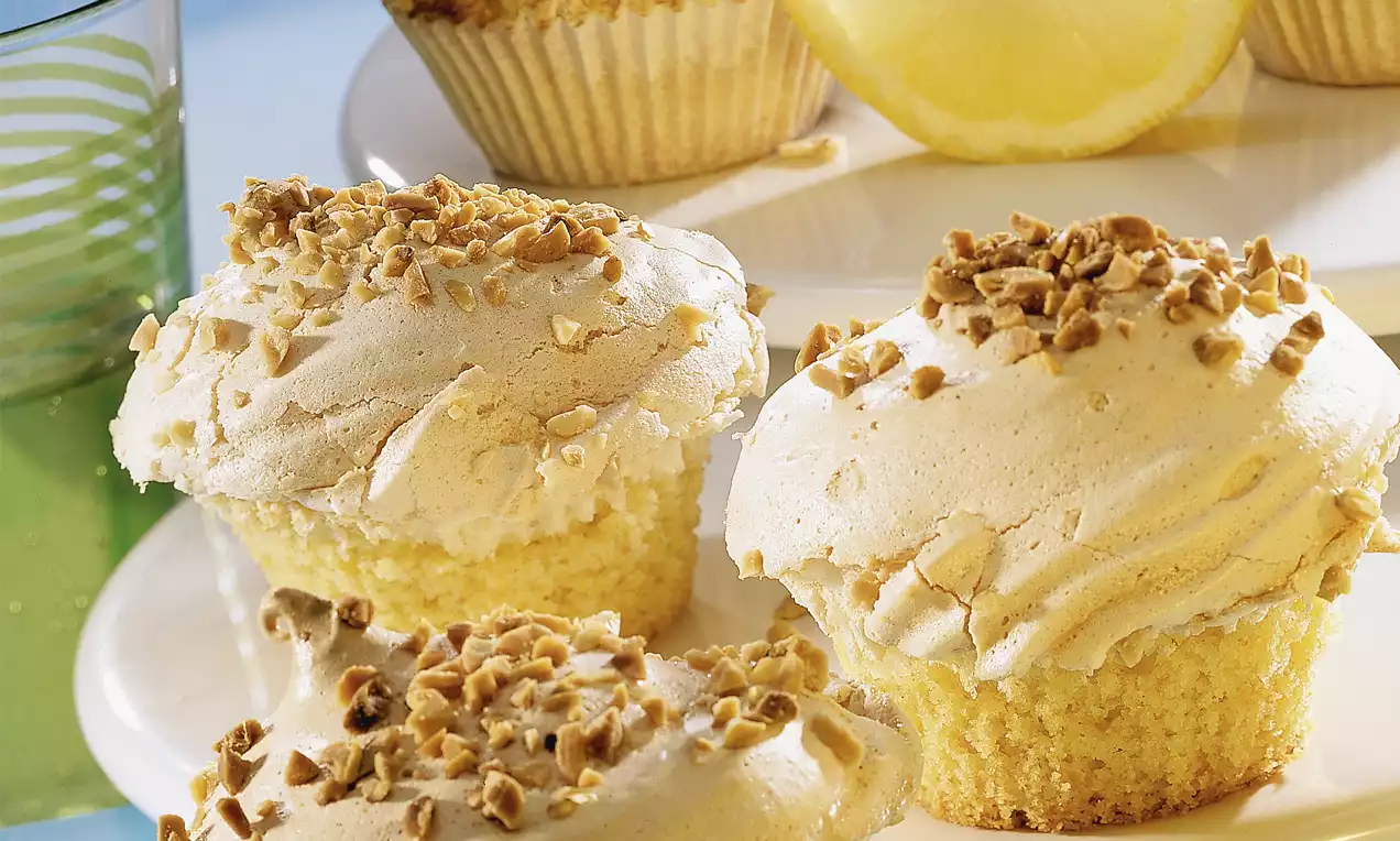 Helle Muffins mit locker cremigem Topping und gehackten Nüssen, auf einem weißen Teller neben einer halben Zitrone angerichtet